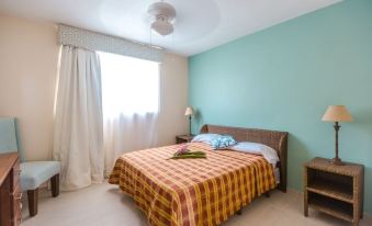 a well - lit bedroom with a white ceiling fan , green walls , and a bed dressed in orange and red plaid sheets at Beachcomber at Las Canas