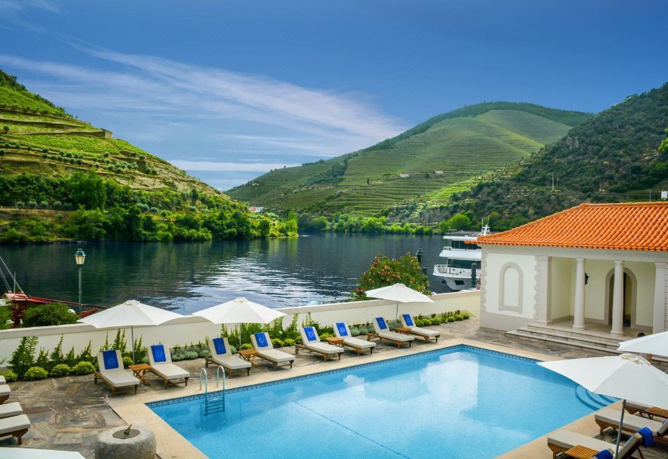 a beautiful outdoor pool area with a swimming pool , sun loungers , umbrellas , and a serene lake view at The Vintage House - Douro