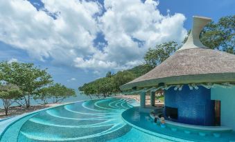 a large blue pool with a thatched roof structure is surrounded by trees and water at Island Escape Burasari