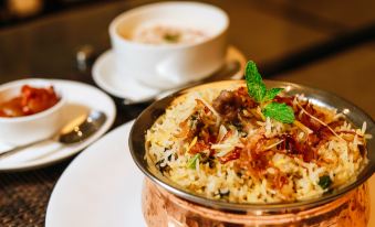 a bowl of rice and meat in a copper bowl on a white plate , accompanied by two cups of tea at Silver Spring
