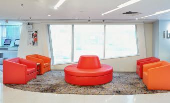 In the waiting room, there are two chairs, an orange couch, and a table in front at Ibis Hong Kong North Point