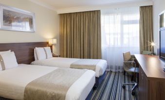 a hotel room with two beds , white linens , and gold curtains , along with a window and a desk at Holiday Inn Ipswich