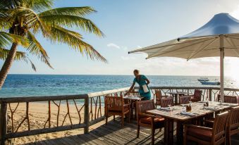 a man in a blue shirt is standing at a table on a wooden deck overlooking the ocean at Castaway Island Fiji