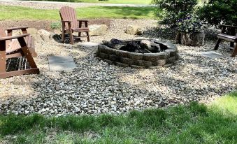 a backyard with a fire pit surrounded by rocks and a wooden chair placed in front of it at Amish Country Comfort