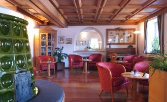 a cozy living room with wooden floors , red chairs , and a fireplace , decorated for the holiday season at Hotel Alpino