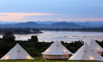 a group of white tents is set up in a grassy field near a body of water at Chiangkhan River Green Hill