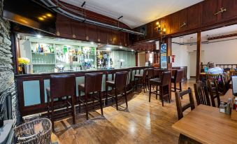a modern bar with wooden furniture , including a long counter and several stools , and an extensive collection of liquor bottles at Grapes Hotel, Bar & Restaurant Snowdonia Nr Zip World