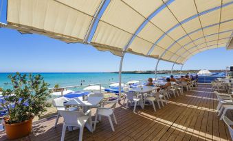 an outdoor dining area near the beach , with tables and chairs set up for guests to enjoy a meal at VOI Arenella Resort