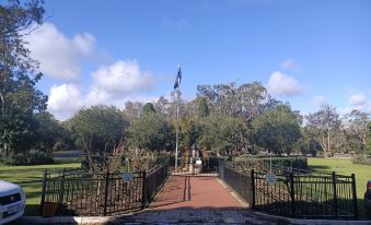 a park entrance with a black wrought - iron fence and a flagpole flying a flag , surrounded by trees at Yanchep Inn