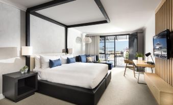 a large , modern bedroom with a white bed and a view of the ocean through a window at Tradewinds Hotel and Suites Fremantle