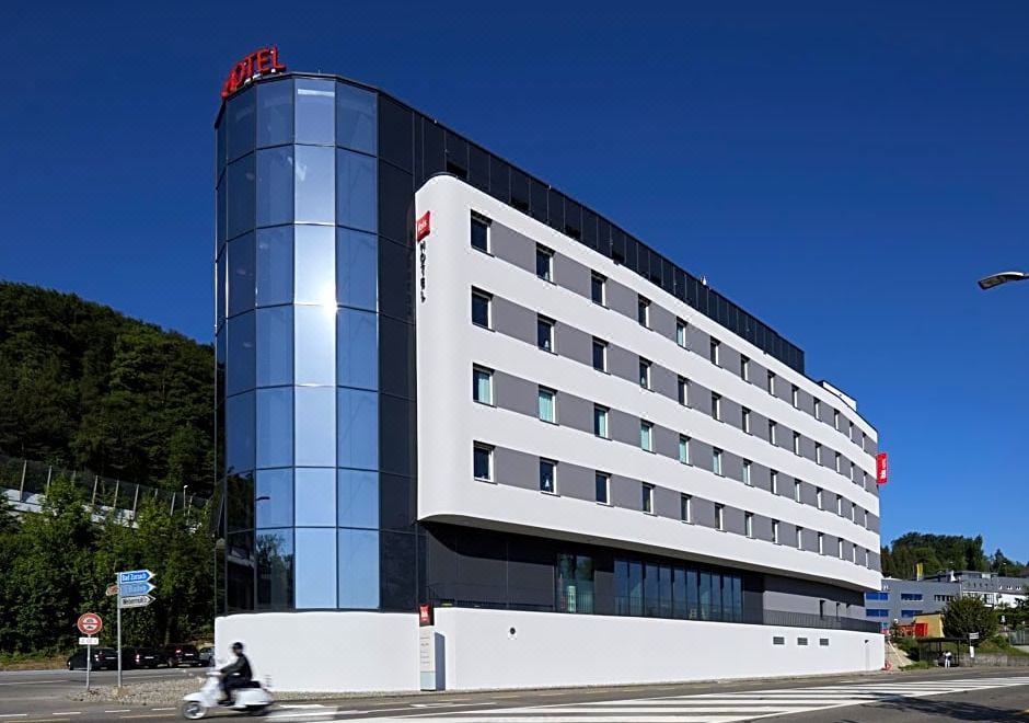 a large white building with a blue exterior and red signage is situated on a street corner at Ibis Baden Neuenhof