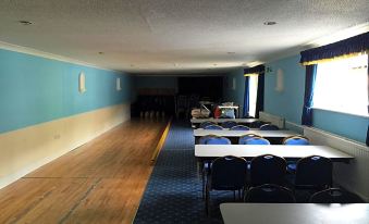 a long , empty hallway with blue walls and wooden floors , featuring rows of tables and chairs at The Old Pound Inn