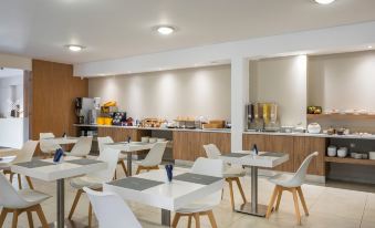 a modern dining area with white chairs and tables , a counter , and a large window at Sea View Hotel & Apartments