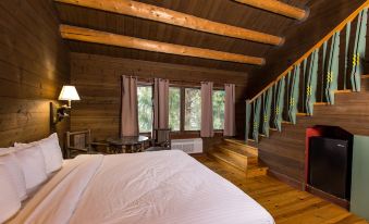 a bedroom with wooden walls and ceiling , a bed , dresser , lamp , and curtains near a window at Drummond Island Resort & Conference Center
