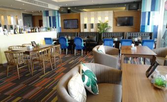 a modern lounge area with blue and gray chairs , wooden tables , and a bar area at Chaisaeng Palace Hotel