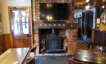 a cozy dining area with a wooden table , chairs , and a large television mounted on the wall above a brick fireplace at The Westgate