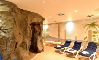 a cozy indoor space with two blue lounge chairs placed in front of a large rock wall , creating a relaxing atmosphere at Hotel Alexandra