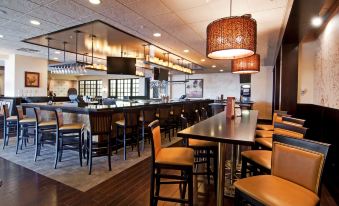 a modern bar with wooden floors , black tables , and chairs , large windows , and hanging lights at Wyndham Minneapolis South/Burnsville