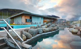 a large outdoor pool surrounded by rocks , with a building in the background and clouds in the sky at Hotel Selfoss