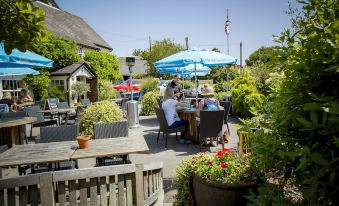 a group of people enjoying a meal at an outdoor restaurant with umbrellas and potted plants at The Cricketers Clavering