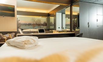 a modern bedroom with a large bed and a desk area , reflecting the view of a swimming pool and mountains outside at Hotel Pineta