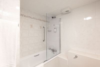 a modern bathroom with white tiles , a bathtub , and a shower area equipped with a glass door at Village Hotel Liverpool
