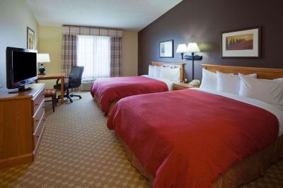 a hotel room with two beds , each made with red linens and a wooden headboard , along with a window and desk at Country Inn & Suites by Radisson, Watertown, SD