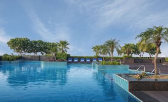 a large swimming pool with blue tiles and palm trees surrounding it under a clear sky at Radisson Blu New Delhi Dwarka