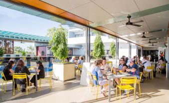 a group of people sitting at outdoor dining tables in a restaurant , enjoying their meals and each other 's company at Rydges Palmerston - Darwin, an EVT hotel