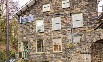 a large stone building with a blue sign on the side , situated in a residential area at Grapes Hotel, Bar & Restaurant Snowdonia Nr Zip World