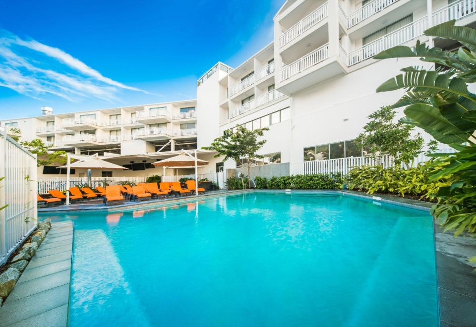 a large swimming pool with orange lounge chairs and umbrellas in front of a white building at Airlie Beach Hotel