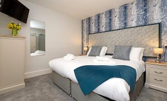 a large bed with a blue blanket and white sheets is in a room with gray flooring at Portbyhan Hotel