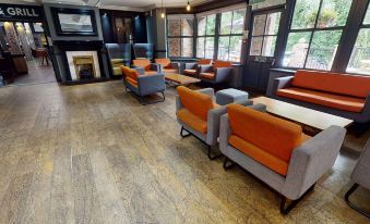 a large room with a wooden floor and orange and gray chairs arranged around a fireplace at Village Hotel Liverpool