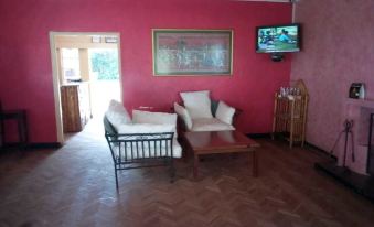 a living room with a red wall , wooden floor , and white furniture , including two couches and a tv at Spice Garden
