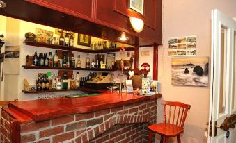 a cozy bar with red brick walls , a wooden bar counter , and various liquor bottles on shelves at Acorns Guest House