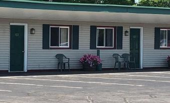 a motel with a row of parked cars and chairs outside , surrounded by trees and flowers at The Lancaster Motel