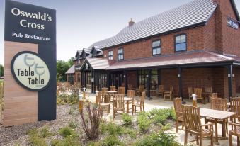 "a brick building with a sign that says "" campagnolo 's alfresco restaurant "" and wooden chairs around a table" at Oswestry