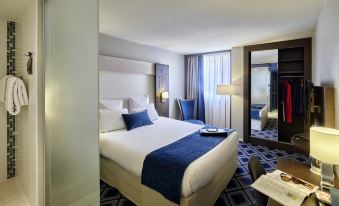 a large bed with white linens and blue accents is in a room with a chair , lamp , and other furniture at Hôtel Mercure Chartres Centre Cathédrale