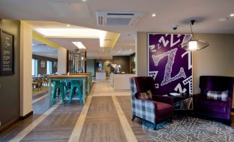 a modern hotel lobby with wooden flooring , a purple chair , and a large painting on the wall at Premier Inn Ulverston