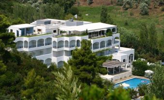 a large , white building with multiple balconies and a swimming pool surrounded by lush greenery at Radisson Resort Skiathos