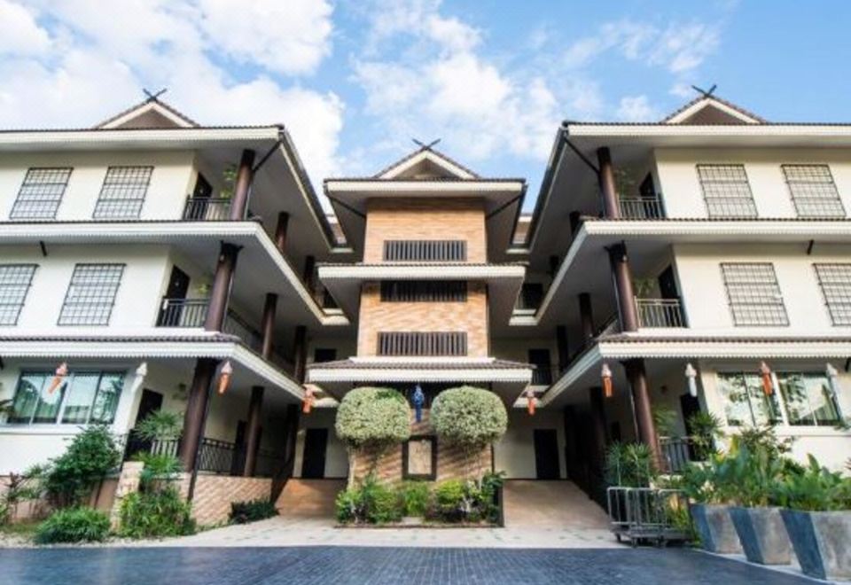 a large , multi - story building with a sloping roof and multiple balconies , surrounded by trees and greenery at Diamond Park Inn Chiangrai & Resort