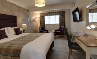 a large bed with a white comforter is in the middle of a room with two purple chairs , a window , and a desk at Manor House Hotel & Spa, Alsager
