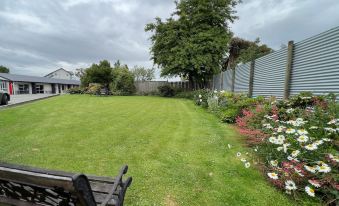 a lush green lawn with a wooden bench in the background , surrounded by trees and flowers at Cedar Lodge Motel