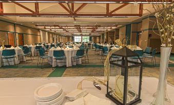 a large banquet hall with multiple tables set up for a formal event , including plates , silverware , and centerpieces at General Butler State Resort Park