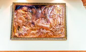 a large copper relief depicting a battle scene is displayed in a gold frame on a white wall at Hotel Cosmos