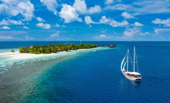 a white sailboat floating in the ocean , surrounded by clear blue water and a sandy beach at Mirihi Island Resort