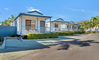 a row of small white houses with blue trim , situated on a street lined with trees and bushes at Discovery Parks - Townsville