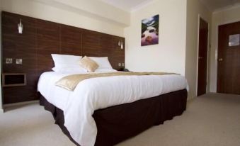 a large bed with white sheets and a brown headboard is in a room with a painting on the wall at The Royal Hotel