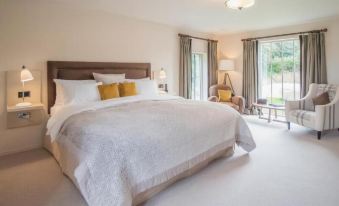 a large , white bed with a brown headboard is in a bedroom with two windows and a chair at The Plume of Feathers