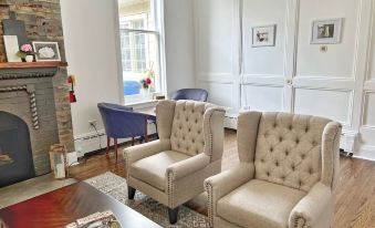 a living room with two beige armchairs , a coffee table , and a brick fireplace , all situated in front of a large window at Inn at the Falls